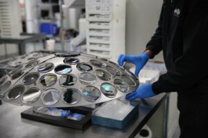 Man with blue gloves moving lenses in optical lab