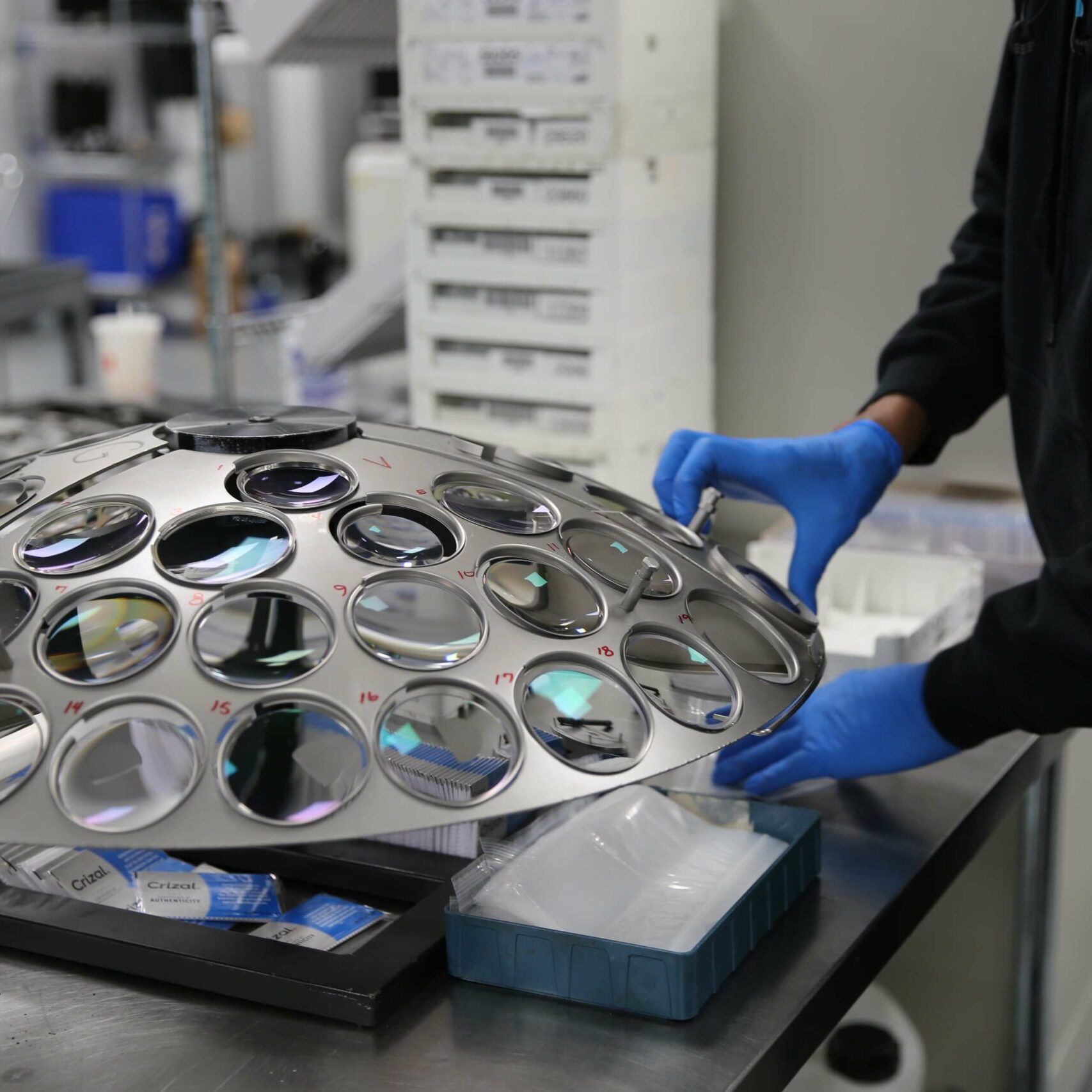 Man with blue gloves moving lenses in optical lab